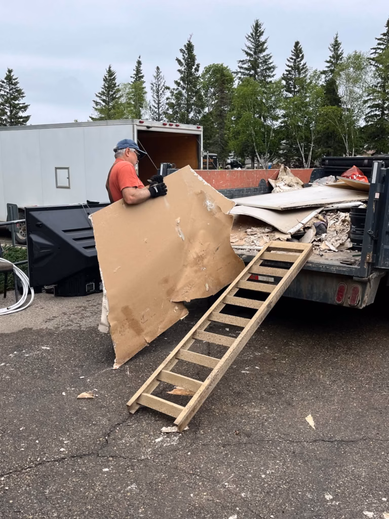 A man throwing water damaged drywall into a dumpster