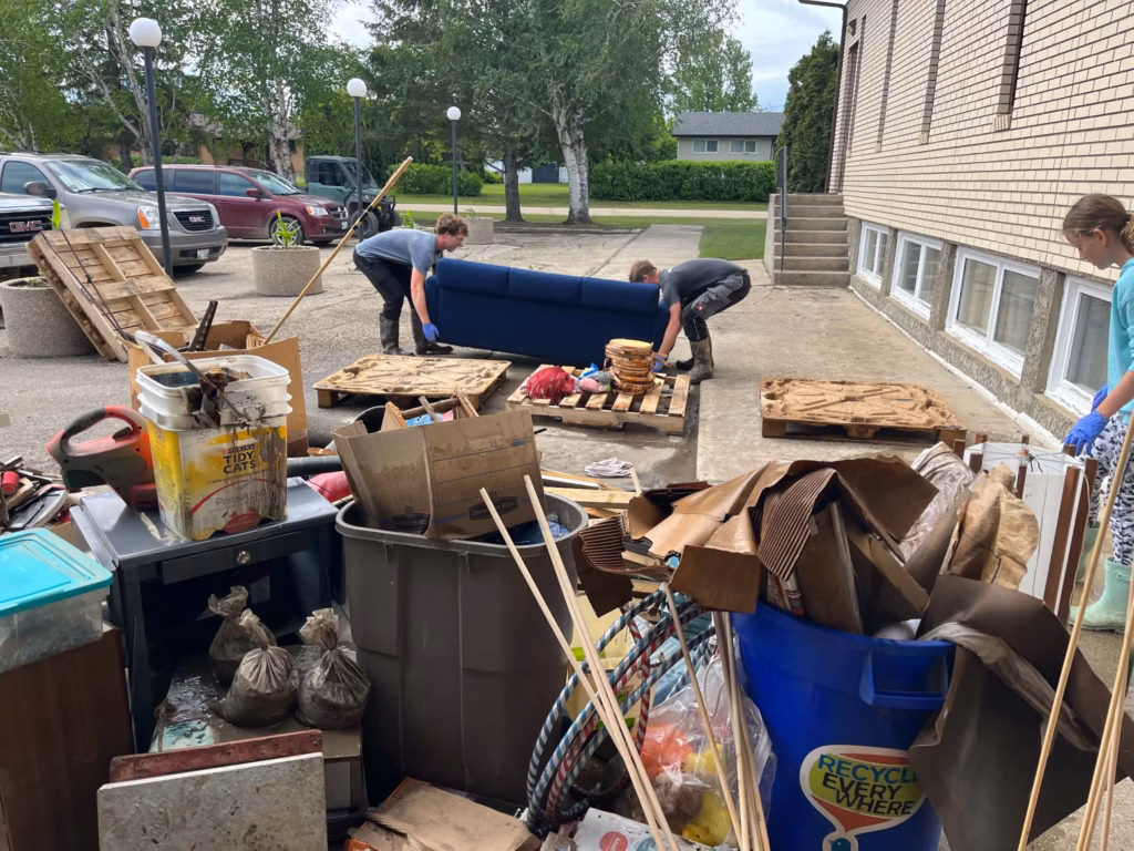 Two men carrying a water damaged couch outside surrounded by other water damaged items